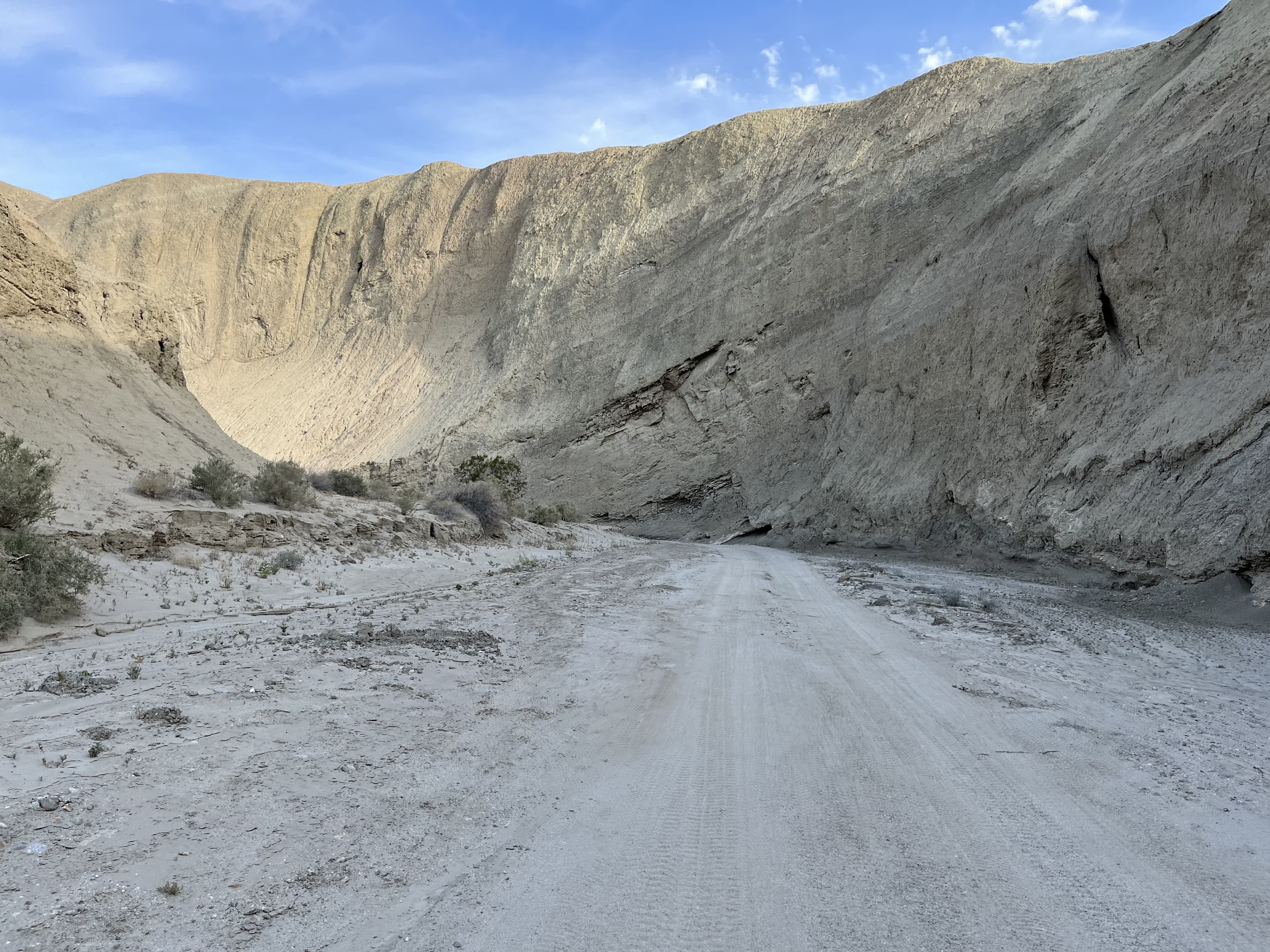 Sandy road cutting between tall, smooth mud canyon walls